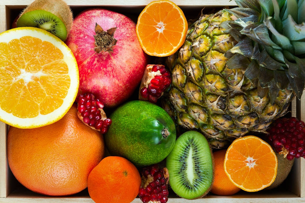 Close up healthy food in wooden tray:  pineapple, orange, tangerine, kiwi, pomegranate and grapefruit. Flat lay. Top view - Photo, Image