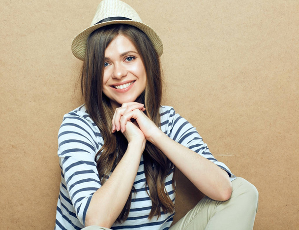 woman wearing striped shirt and hipster hat sitting near beige wall background  - Valokuva, kuva