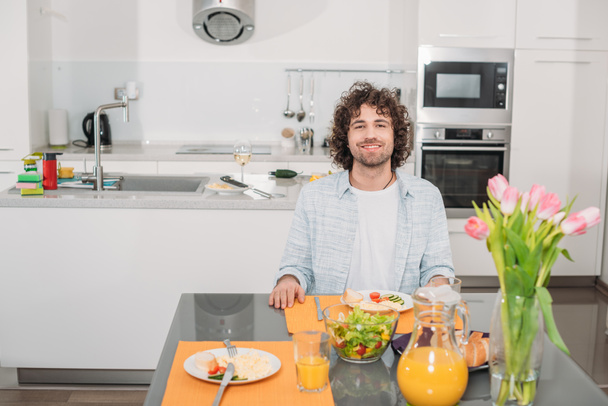 smiling man sitting at table with food and looking at camera - Foto, Bild