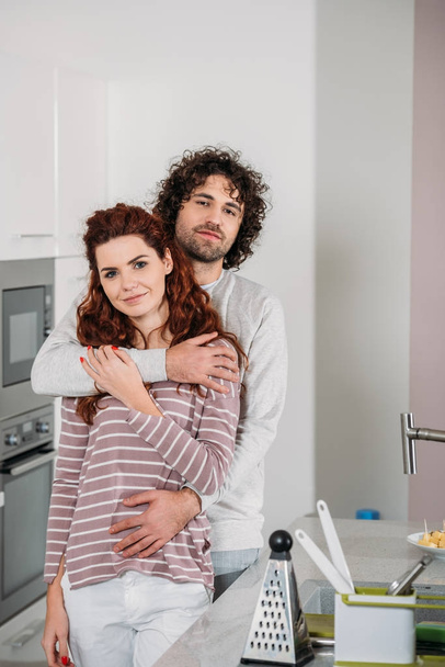 novio abrazando novia en la cocina y mirando a la cámara
 - Foto, Imagen