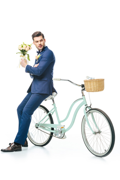 stylish groom with wedding bouquet leaning on retro bicycle isolated on white - Фото, изображение