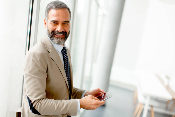 Handsome mature businessman with mobile phone in the office - Photo, Image