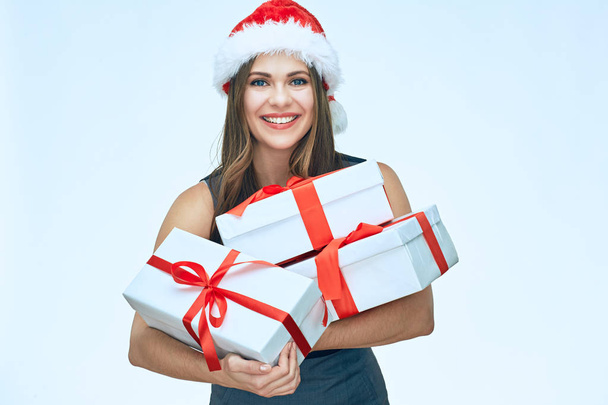 happy businesswoman in grey dress and red santa hat holding Christmas gifts - Foto, Imagen