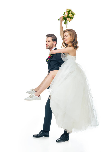side view of happy bride and groom piggybacking together isolated on white - Φωτογραφία, εικόνα
