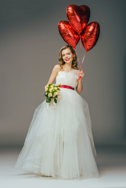 smiling bride in wedding dress with heart shaped balloons and bouquet of flowers - Foto, Imagem