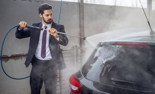 handsome stylish young bearded man in suit washing car at the manual car washing self-service station - Photo, Image
