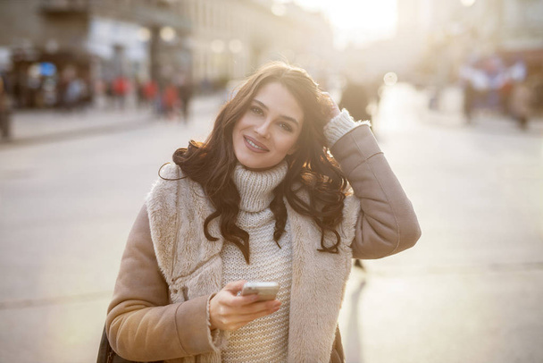 glücklich schöne Frau im Wintermantel mit Smartphone an der Stadtstraße - Foto, Bild