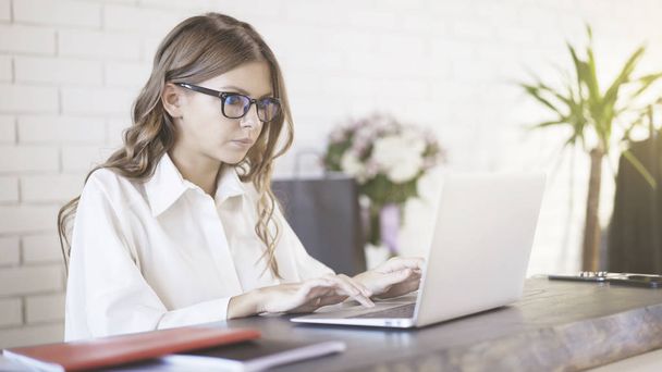 Vue latérale d'une jeune belle femme portant des lunettes tapant sur son ordinateur portable au bureau
. - Photo, image