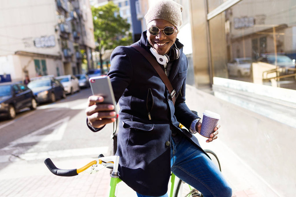 Красивий молодий чоловік використовує мобільний телефон і фіксований велосипед на вулиці
. - Фото, зображення