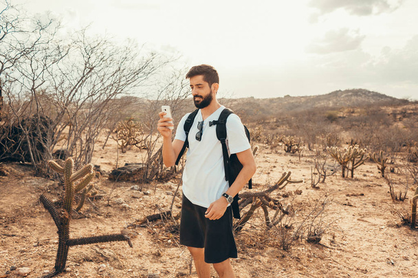 Young man on the trip. Traveler with smart phone in the hand is resting on the top of mountain at the sunset. - Foto, Imagen