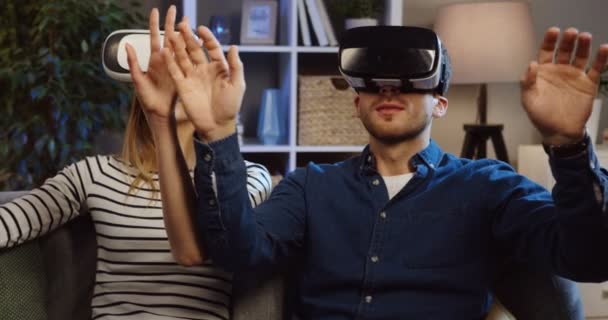Young couple sitting on the couch in the living room in VR glasses and having VR headset, scrolling and taping in the air. Evening time. Close up. Portrait. Inside - Záběry, video
