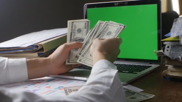 Businessman at workplace counting Many American 100 bills. oncept of salary or making money. Laptop with a green screen on the desk - Footage, Video