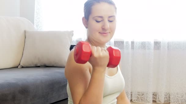 4k closeup footage of young smiling woman exercising and strenghtening hand muscles with dumbbells - Footage, Video