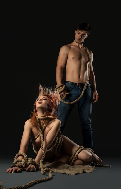 Sexy man and nude girl tied with rope on her knees - 写真・画像