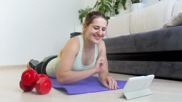 4 k materiał filmowy z piękną, młodą kobietę, oglądanie motywacyjne wideo cyfrowego tabletu podczas ćwiczeń na macie fitness - Materiał filmowy, wideo