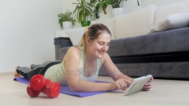 4k zooming in footage of young woman using digital tablet while exercising on fitness mat at home - Filmati, video