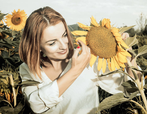 Mooie vrouw is permanent door zonnebloem, vintage filter - Foto, afbeelding