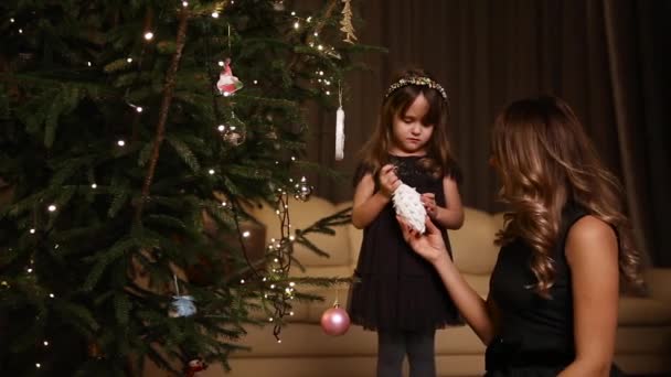 Mutter schenkt ihrer Tochter ein Weihnachtsspielzeug, damit sie am Baum hängt. - Filmmaterial, Video