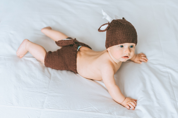 high angle view of infant child in knitted deer costume in bed - Foto, imagen