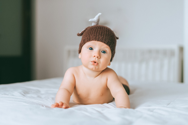 surprised emotional infant child in knitted deer hat in bed - Photo, Image