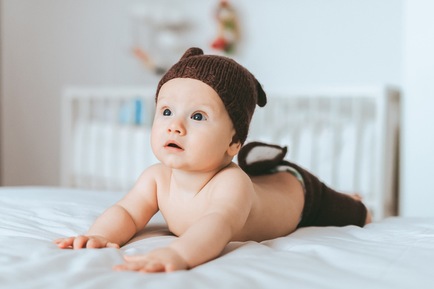 wyrażona niemowlę dziecko w szorty z dzianiny jelenia i kapelusz w łóżku - Zdjęcie, obraz