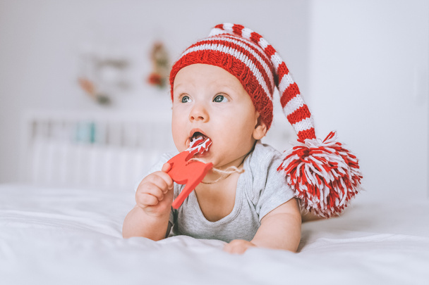 niño pequeño en sombrero de rayas de punto jugando con ciervos de juguete en la cama
 - Foto, imagen