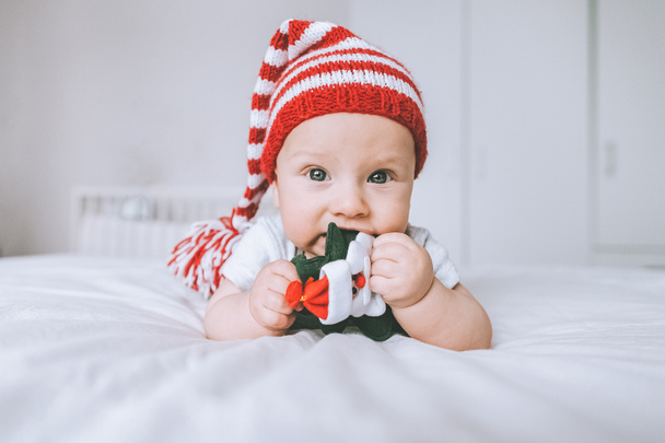 infant child in striped hat playing with toy christmas tree in bed - Foto, imagen