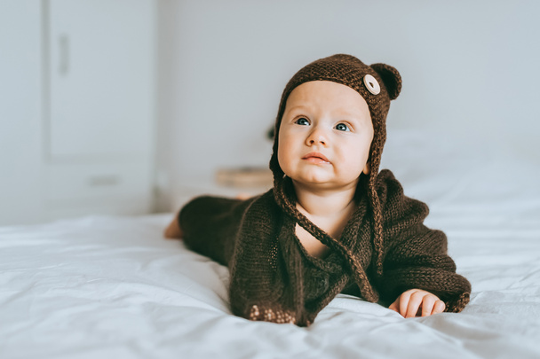 beautiful infant child in brown knitted hat and blanket in bed - Foto, imagen