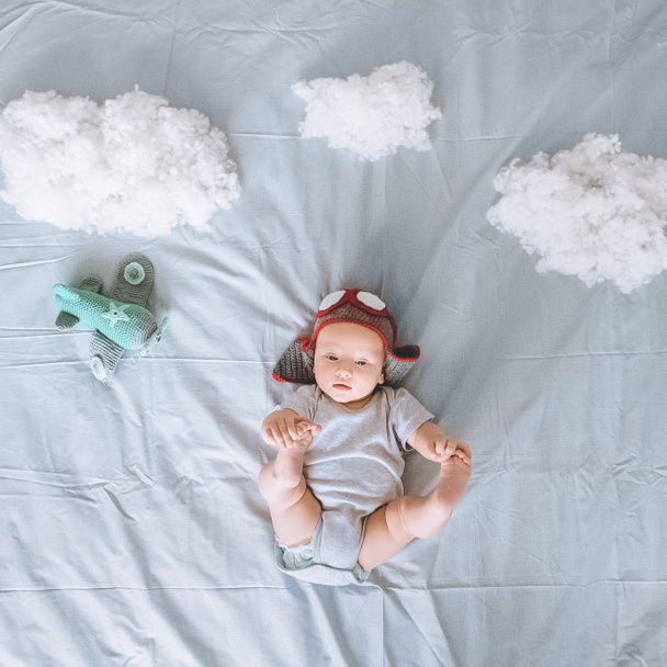 vista superior de niño adorable en sombrero piloto de punto con avión de juguete rodeado de nubes de algodón en la cama
 - Foto, Imagen