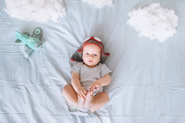 top view of cute infant child in knitted pilot hat with toy plane surrounded with clouds made of cotton in bed - Photo, Image