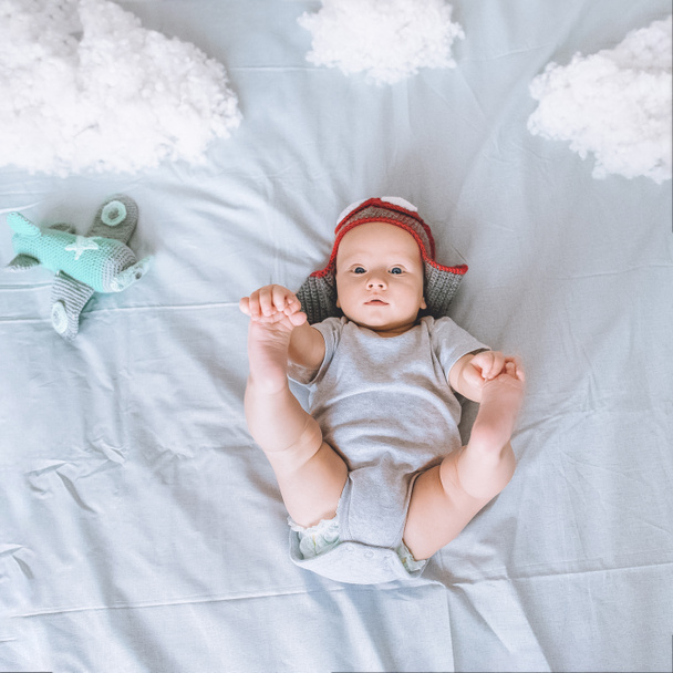 top view of infant child in pilot hat with toy plane surrounded with clouds made of cotton in bed - Photo, Image
