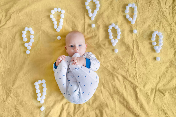 top view of funny infant child surrounded with exclamation marks made of cotton balls in bed looking at camera - Фото, зображення