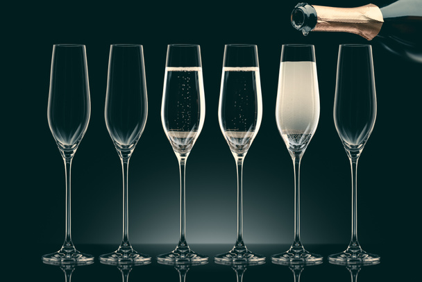 champagne fles gieten in zes transparante glazen op zwart - Foto, afbeelding