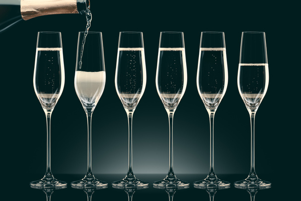pouring champagne from bottle into six transparent glasses on black - Foto, afbeelding