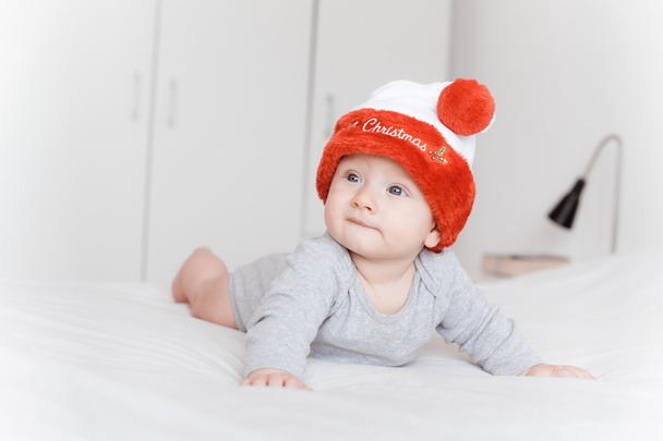 πορτρέτο του όμορφη βρέφος το παιδί με το καπέλο santa ξαπλωμένος στο κρεβάτι και κοιτάζοντας μακριά   - Φωτογραφία, εικόνα