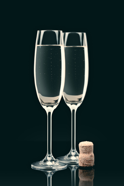 two transparent glasses with calm champagne and cork on table on black - Foto, Bild