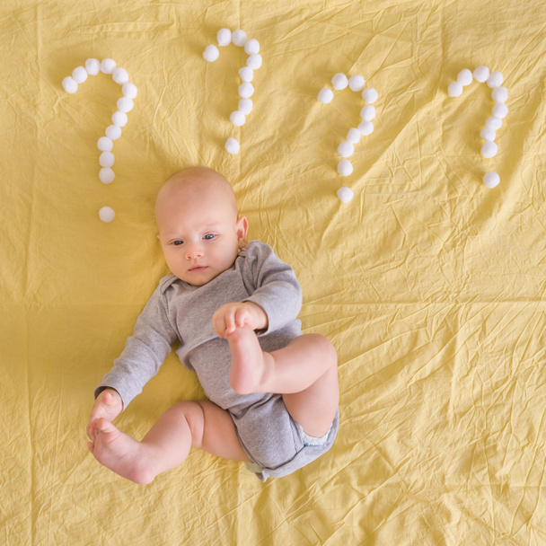 top view of funny infant child lying surrounded with question marks made of cotton balls in bed  - Photo, Image