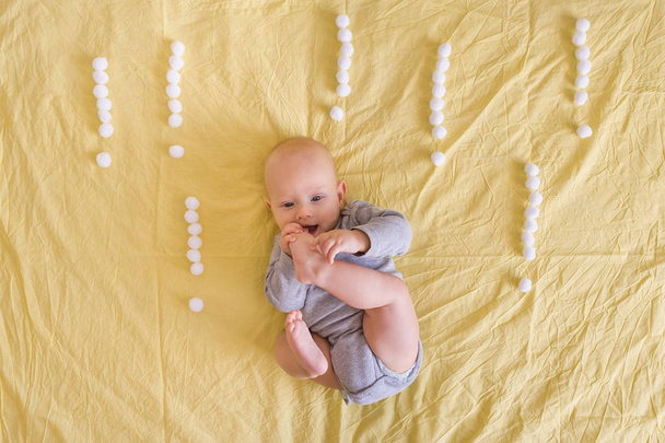 bovenaanzicht van schattig klein kind liggen omringd met uitroeptekens gemaakt van katoenen ballen in bed  - Foto, afbeelding