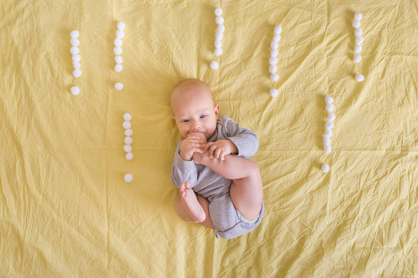 bovenaanzicht van schattige grappige baby kind liggen omringd met uitroeptekens gemaakt van katoenen ballen in bed  - Foto, afbeelding