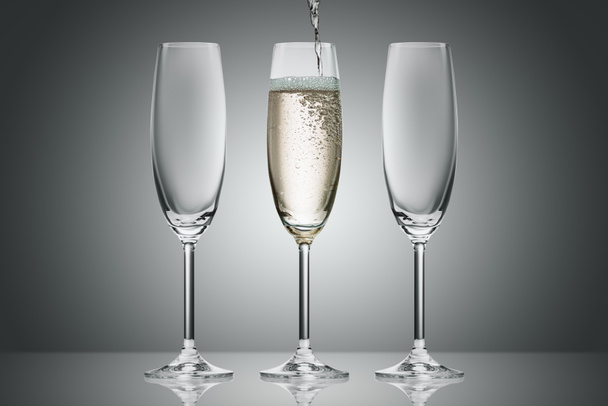 pouring champagne from bottle into three glasses on grey - Фото, изображение