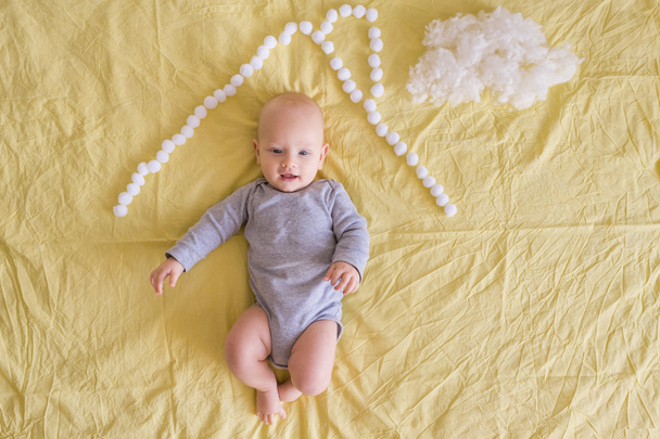 top view of adorable child under house roof made of cotton balls and cotton cloud on bed   - Foto, Bild