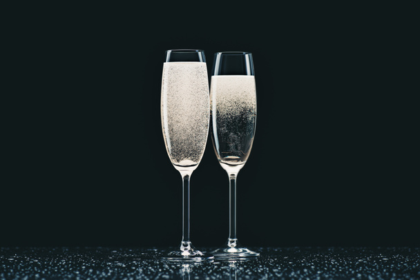 two glasses with champagne with drops on table on black - Photo, Image
