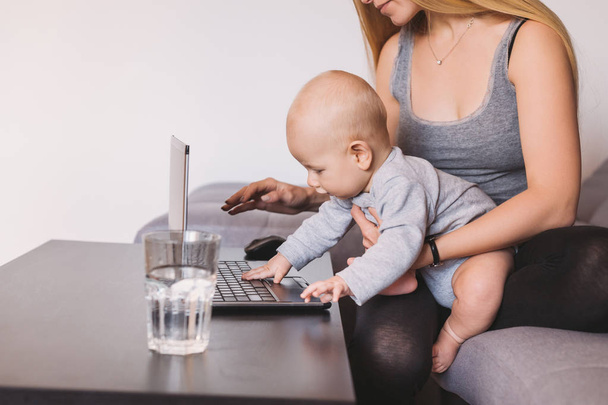tiro recortado de jovem mãe segurando adorável criança infantil usando laptop na sala de estar
  - Foto, Imagem
