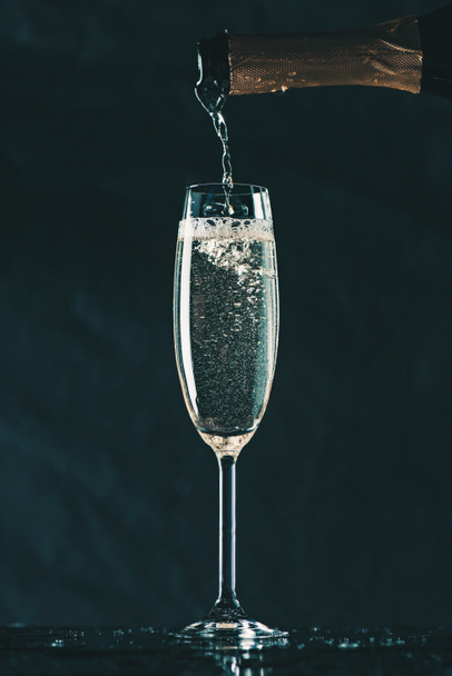 El champán que vierte de la botella en el cristal sobre negro
 - Foto, Imagen