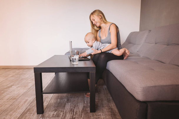 vista lateral de sorrir jovem mãe segurando criança infantil usando laptop na sala de estar
 - Foto, Imagem