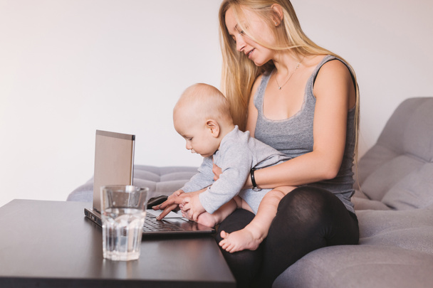 bella sorridente giovane madre che tiene adorabile bambino neonato utilizzando il computer portatile
  - Foto, immagini