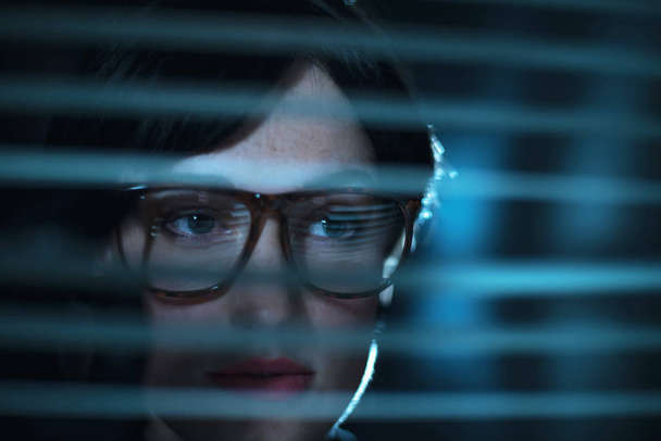  woman in glasses looking through blinds - Foto, afbeelding