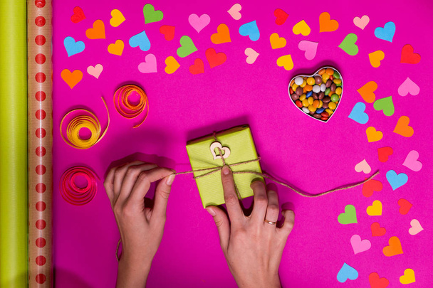 Ystävänpäivä lahja kääre laatikot vaaleanpunainen tausta ja värikäs paperi sydämet ympärillä. Käsintehdyn lahjan prosessi. Luova diy craft harrastus. Lomakoristeet
 - Valokuva, kuva