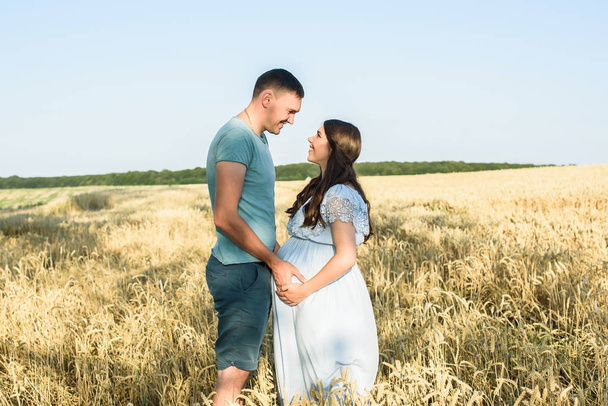Romantic Pregnant couple portrait in a wheat field. Pregnant woman standing with her husband relaxing in nature on a beautiful sunny day - Fotografie, Obrázek