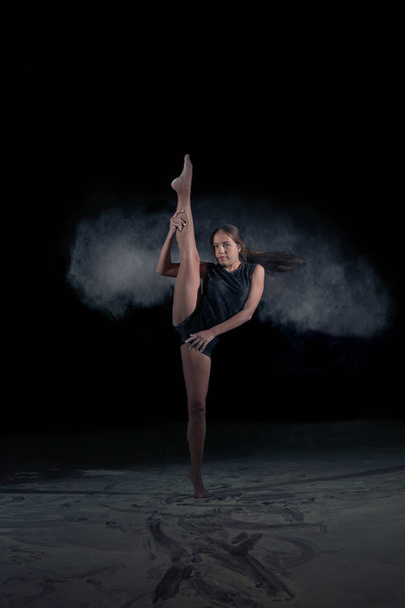 The girl gymnast makes a gymnastic sketch with flying powder. Sport. Dance. - Фото, изображение